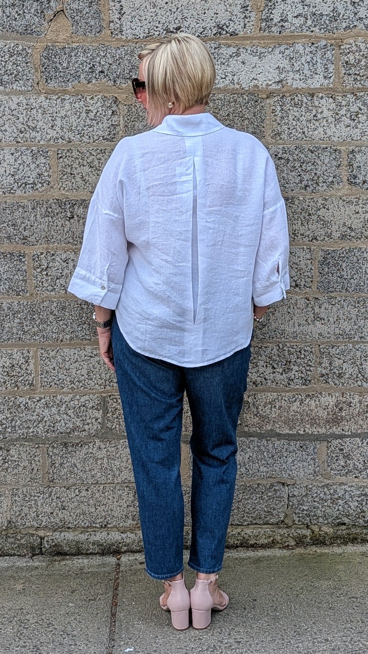 Back View of a white button up shirt, dark blue jeans, and pink flat shoes.
