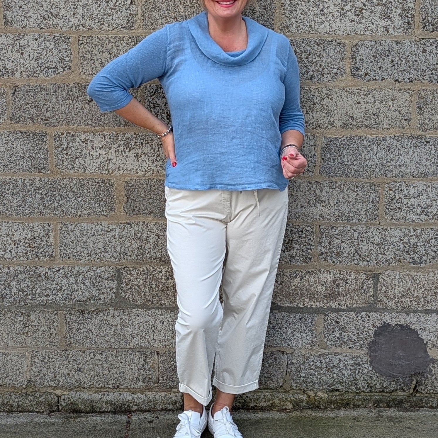 Front View  a light blue cowl neck knit top, cream colorued cropped trousers, white sneakers.