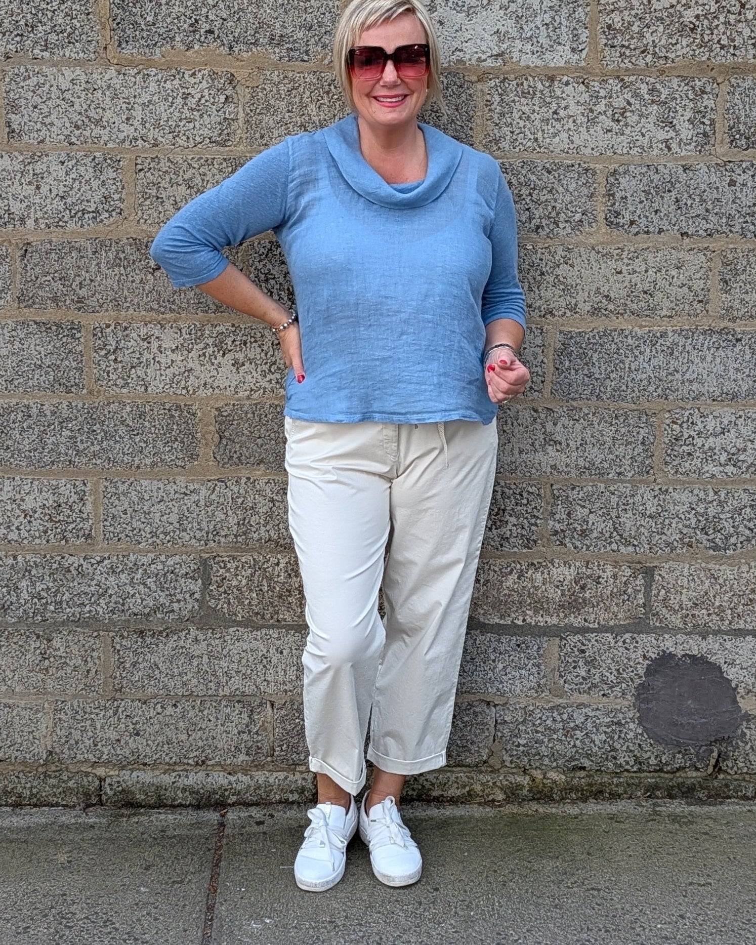 Front View  a light blue cowl neck knit top, cream colorued cropped trousers, white sneakers.