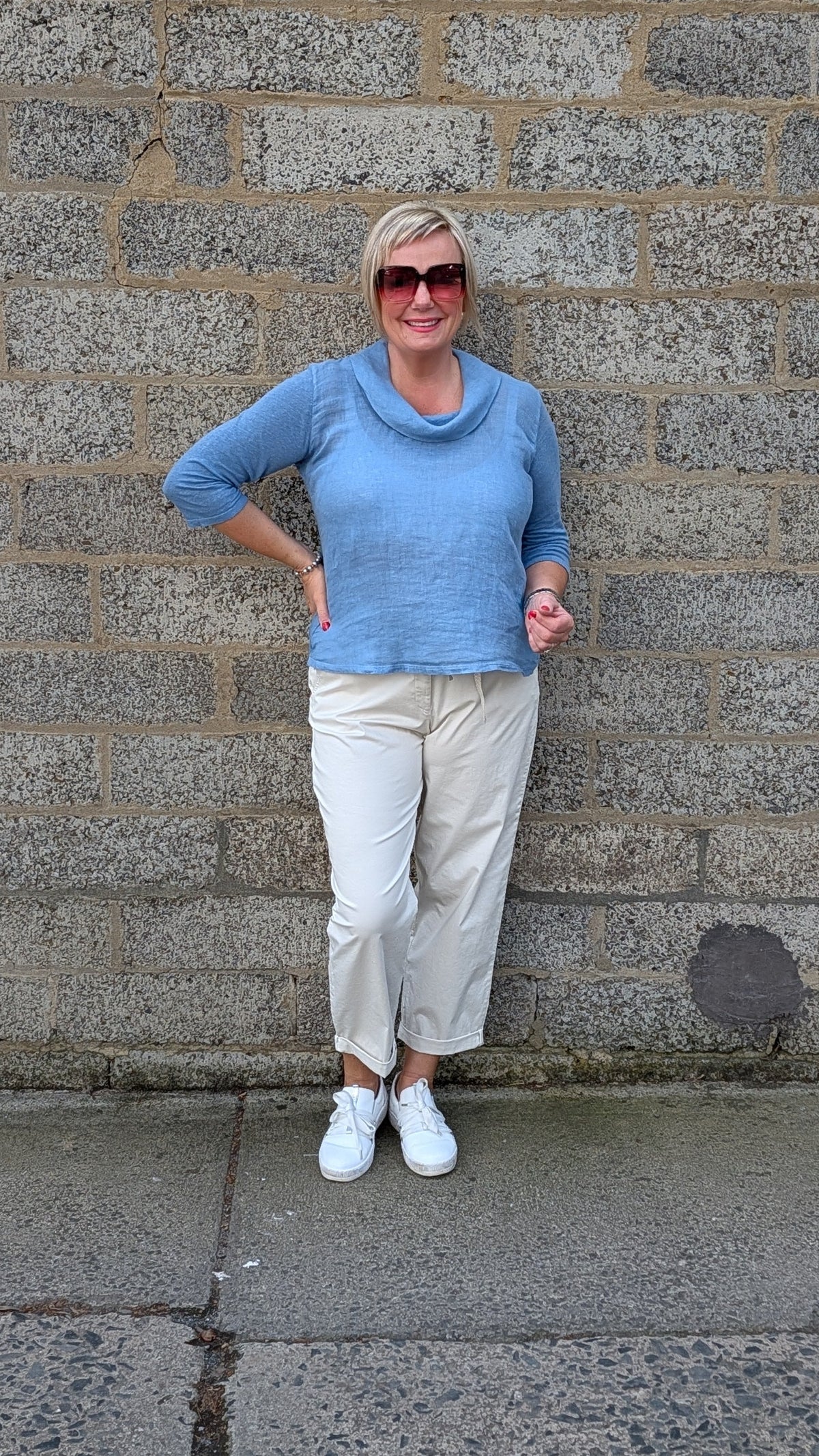 Front View  a light blue cowl neck knit top, cream colorued cropped trousers, white sneakers.