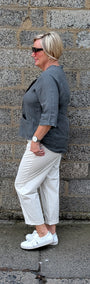 Side view of  a dark grey top, off white cropped trousers, and white sneakers.