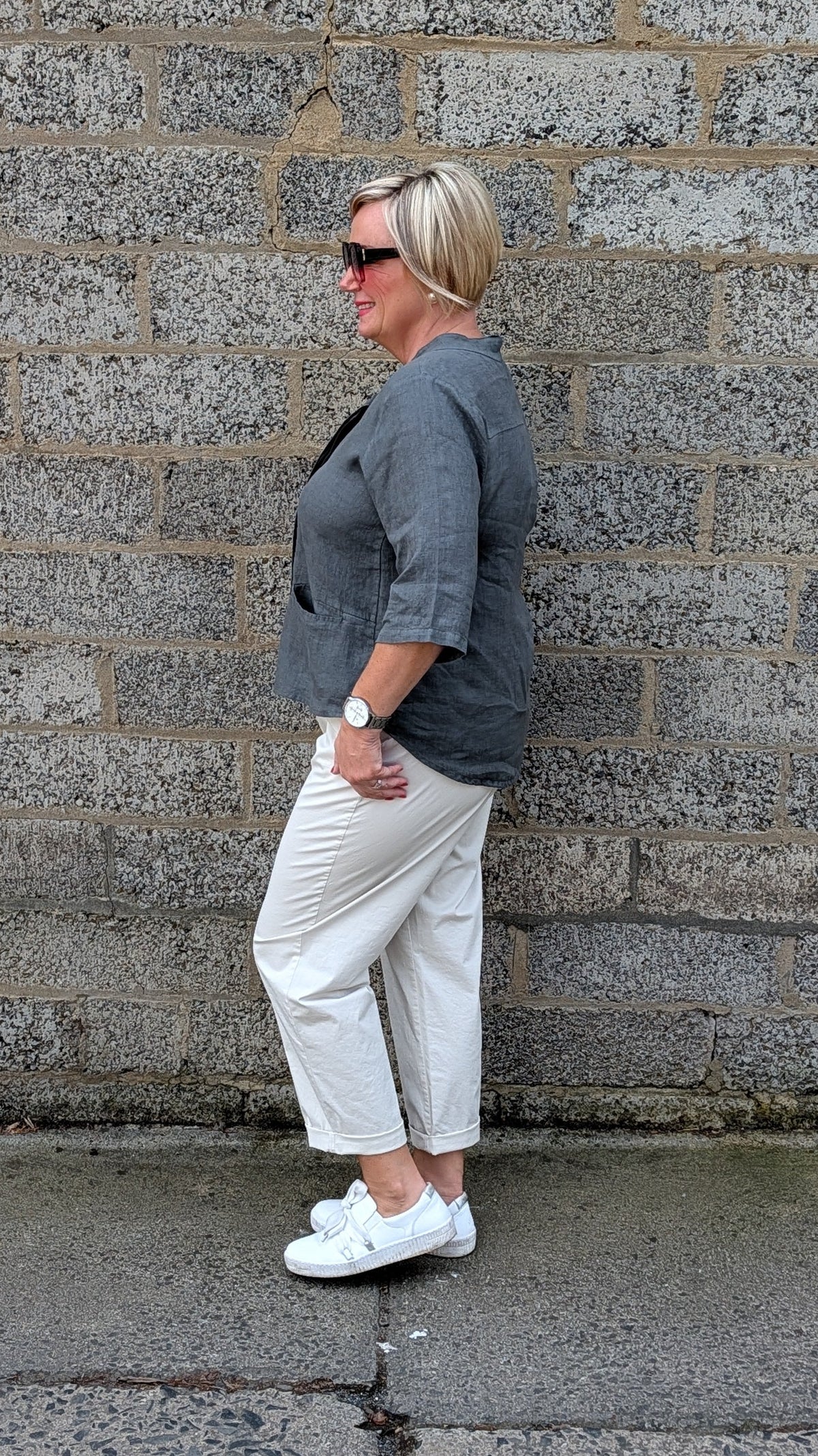 Side view of  a dark grey top, off white cropped trousers, and white sneakers.