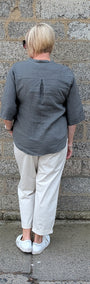 Back View of a dark grey short sleeve button up shirt, off white trousers, and white sneakers.