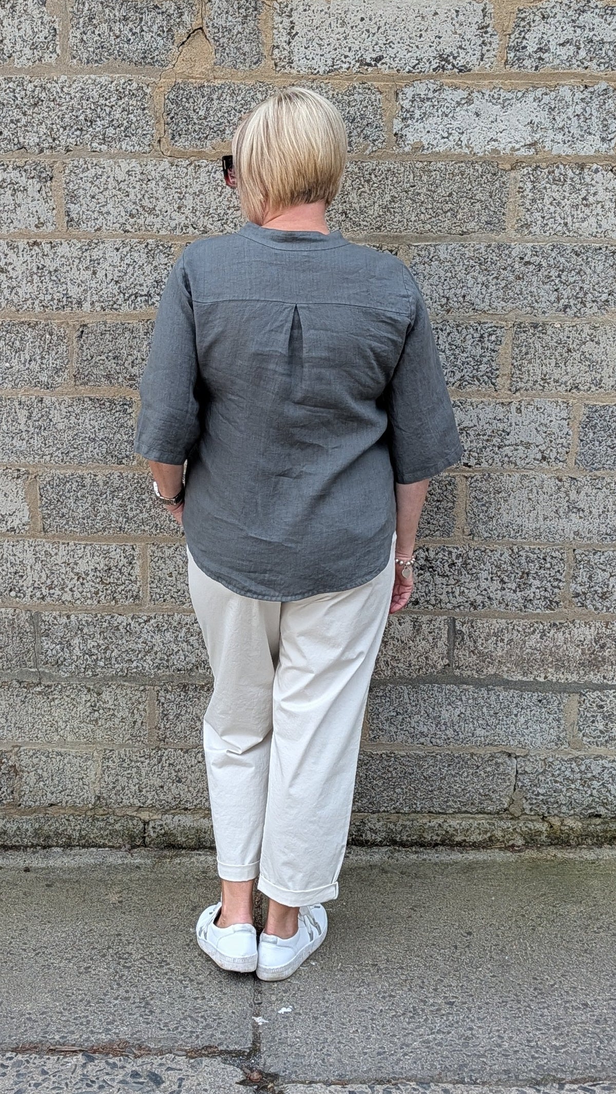 Back View of a dark grey short sleeve button up shirt, off white trousers, and white sneakers.