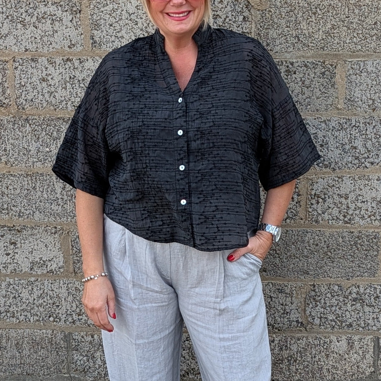 Front View of  a black short sleeve button up shirt, light gray cropped trousers, and white pointed toe heels.