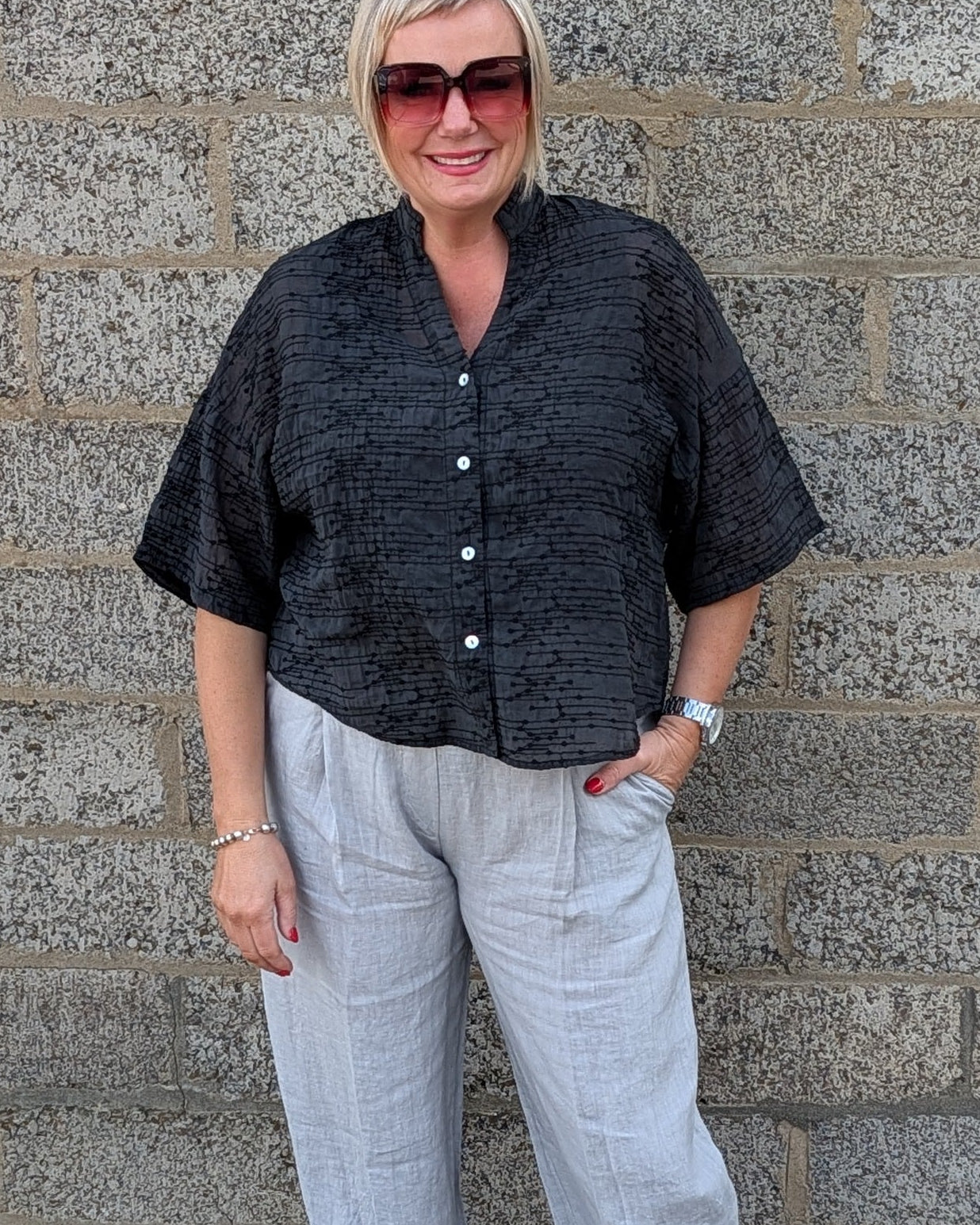Front View of  a black short sleeve button up shirt, light gray cropped trousers, and white pointed toe heels.