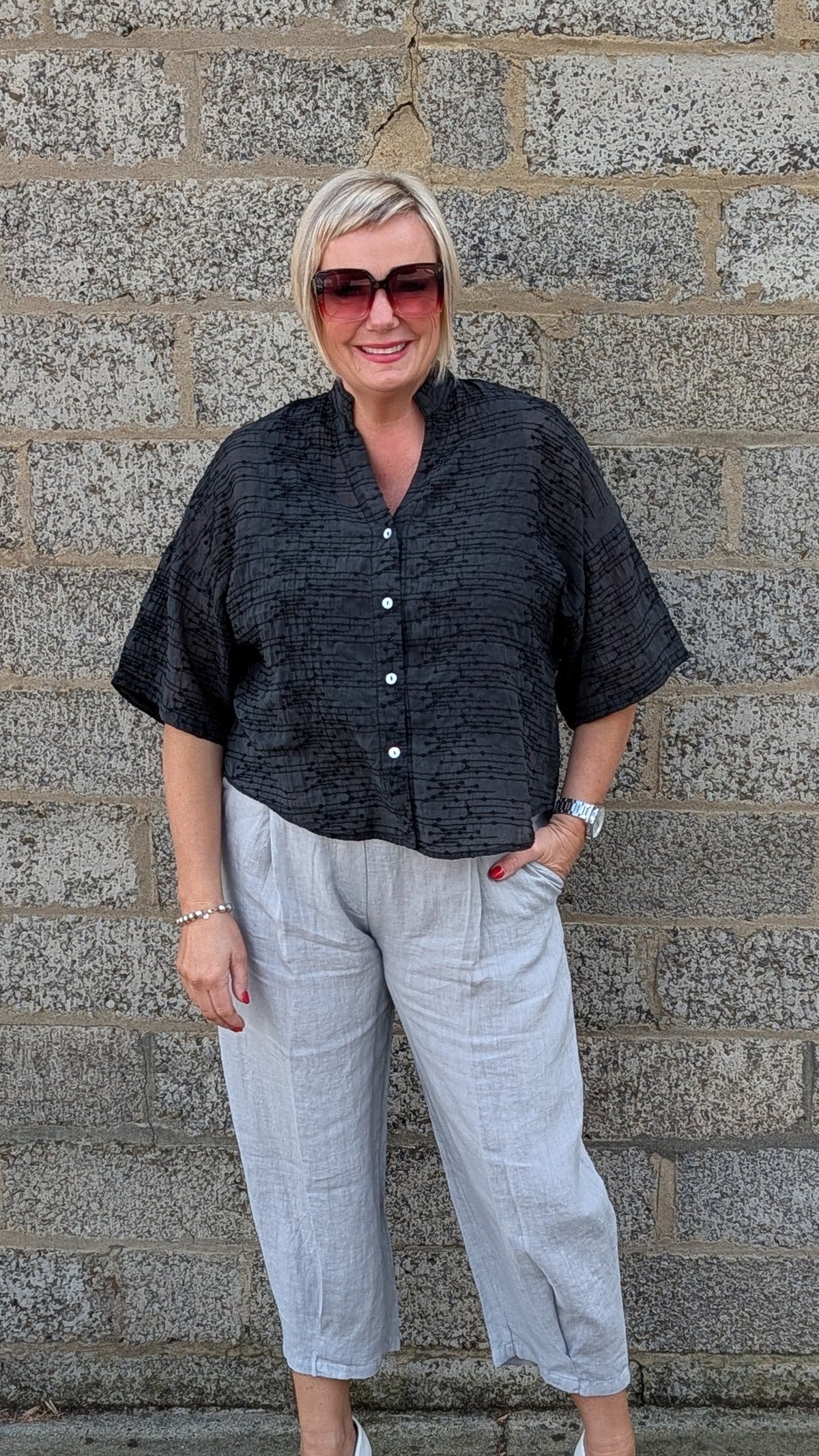 Front View of  a black short sleeve button up shirt, light gray cropped trousers, and white pointed toe heels.