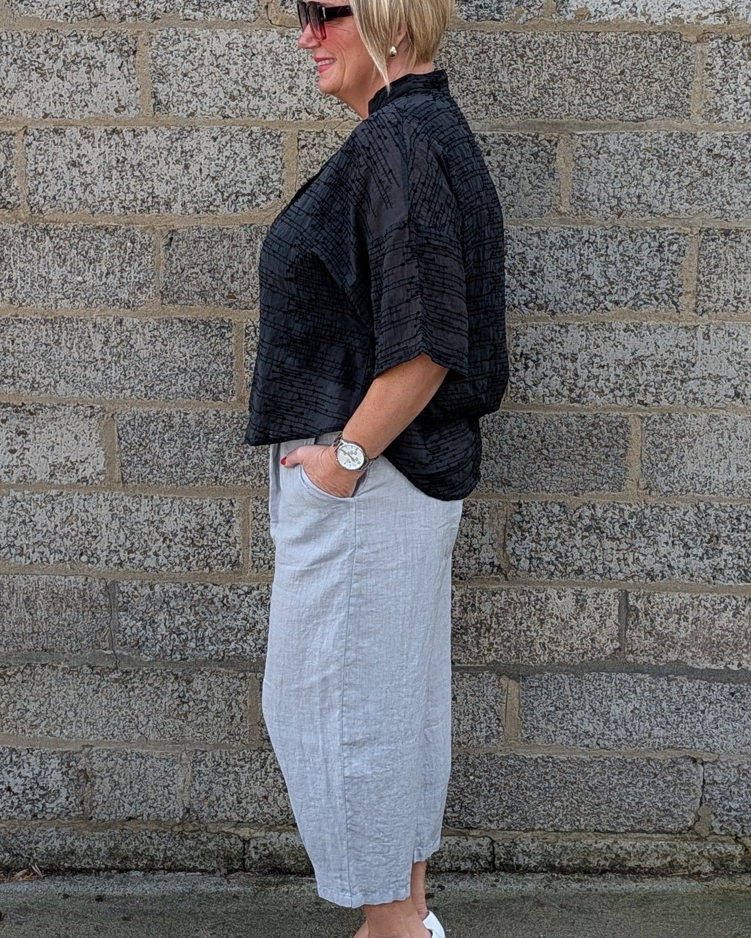 side view of a black textured shortsleeve top, a light black pleated midi shirt  and white pointed-toe flats.