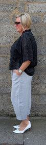 side view of a black textured shortsleeve top, a light black pleated midi shirt  and white pointed-toe flats.