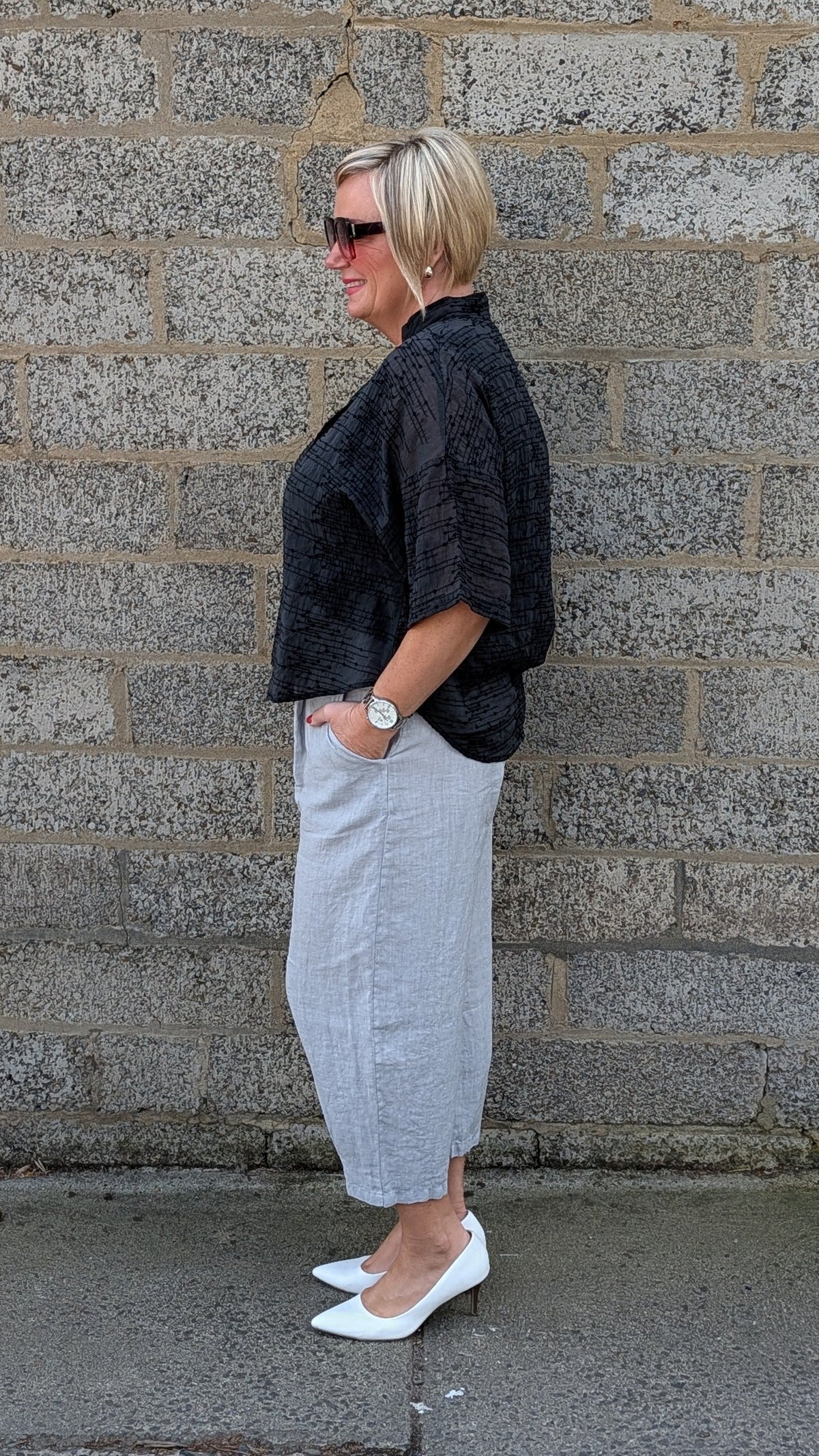 side view of a black textured shortsleeve top, a light black pleated midi shirt  and white pointed-toe flats.