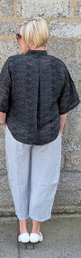 Back view of  a  black textured short sleeve top, light grey cropped pants, and white sneakers.