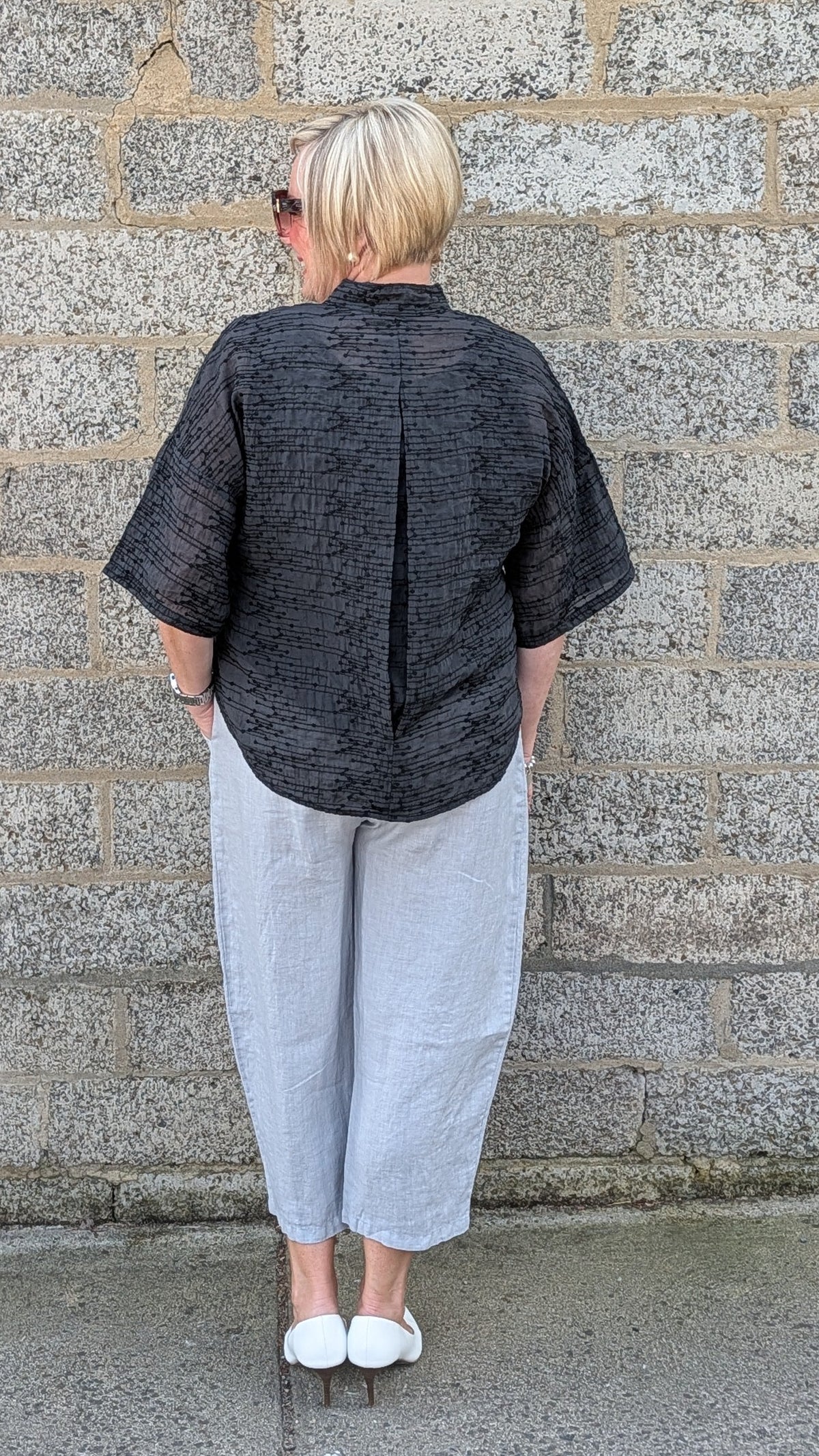 Back view of  a  black textured short sleeve top, light grey cropped pants, and white sneakers.