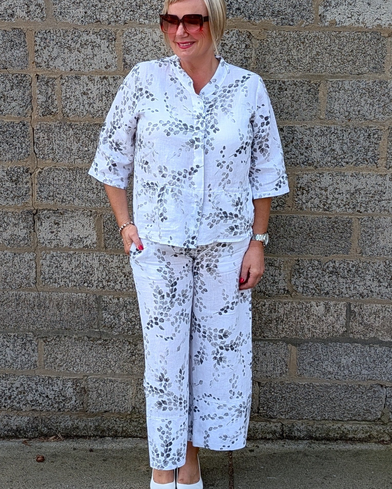 Front view of a white two piece set with a black floral pattern, consisting of a short sleeve button up top and matching wide leg pants.