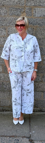 Front view of a white two piece set with a black floral pattern, consisting of a short sleeve button up top and matching wide leg pants.