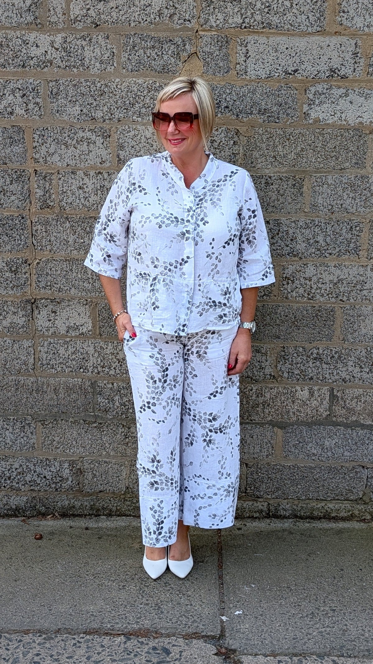 Front view of a white two piece set with a black floral pattern, consisting of a short sleeve button up top and matching wide leg pants.