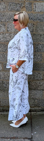 Side view of white shirt with a black floral print and white pointed flats.