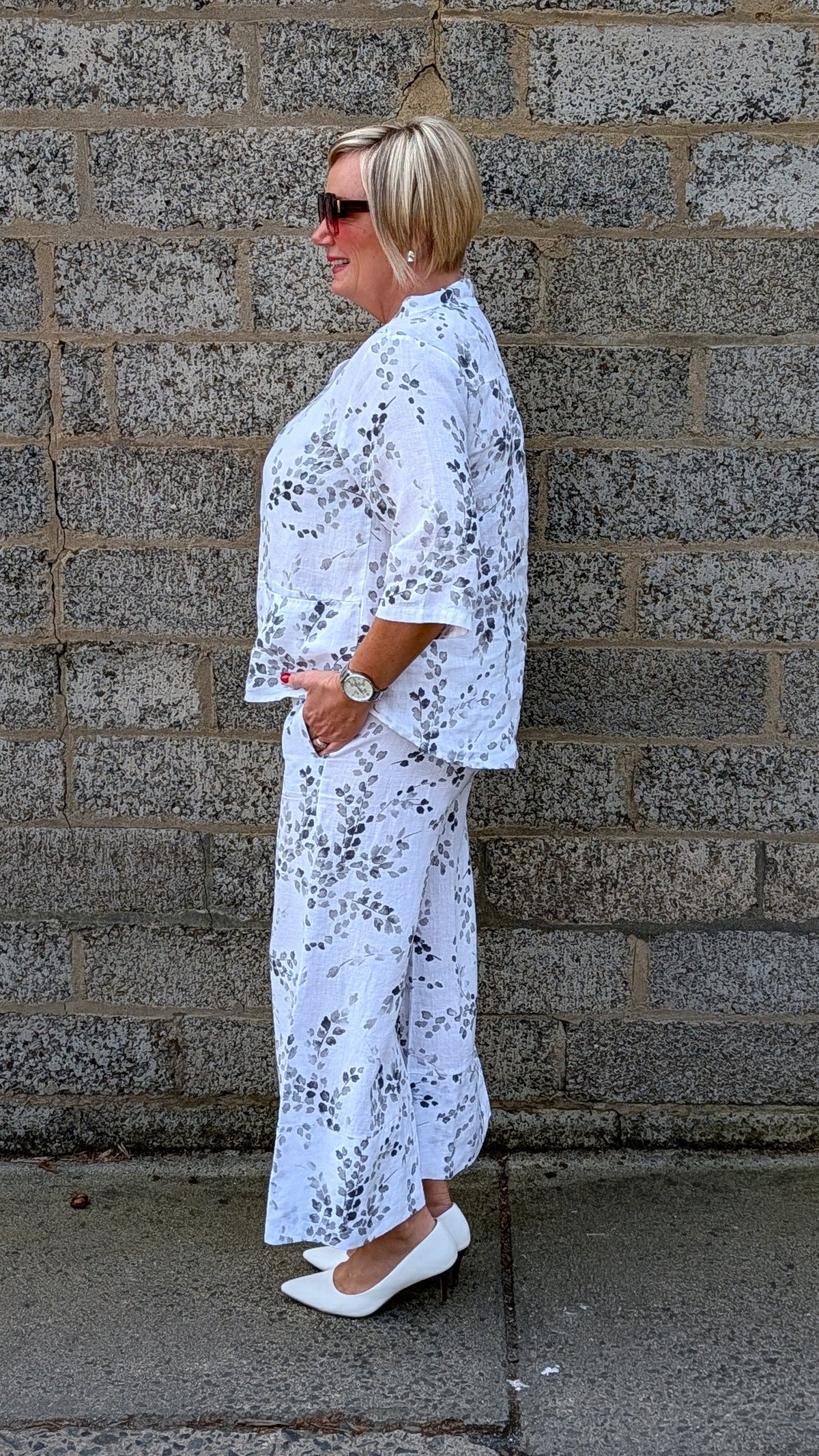Side view of white shirt with a black floral print and white pointed flats.