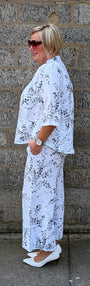 side view wearing a white two piece outfit with a black floral print and white pointed flats.
