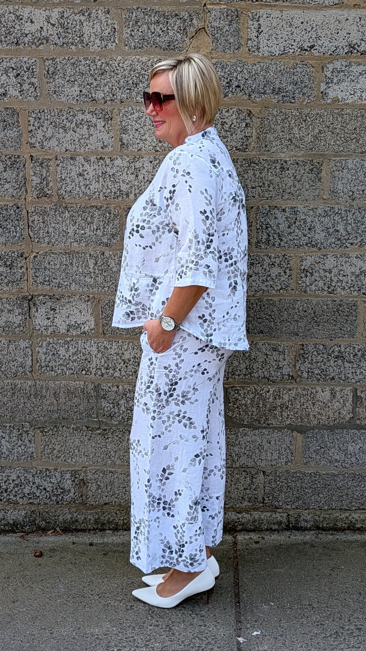 side view wearing a white two piece outfit with a black floral print and white pointed flats.