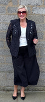  black lace blazer, a white top, black wide-leg pants, and black heels.