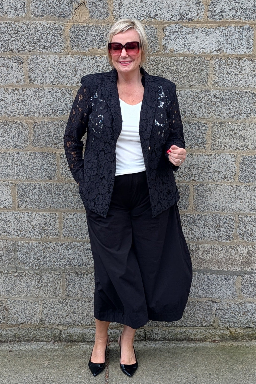  black lace blazer, a white top, black wide-leg pants, and black heels.