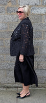  black lace trimmed blazer over a black midi skirt and black heels.