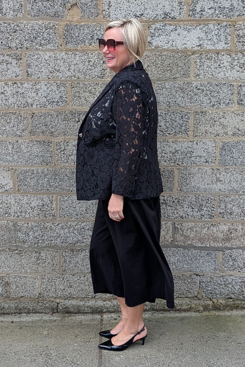  black lace trimmed blazer over a black midi skirt and black heels.