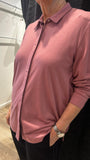 A woman wearing a dusty pink long-sleeve knit button-up shirt with a collar, paired with black trousers, standing in a fitting room.