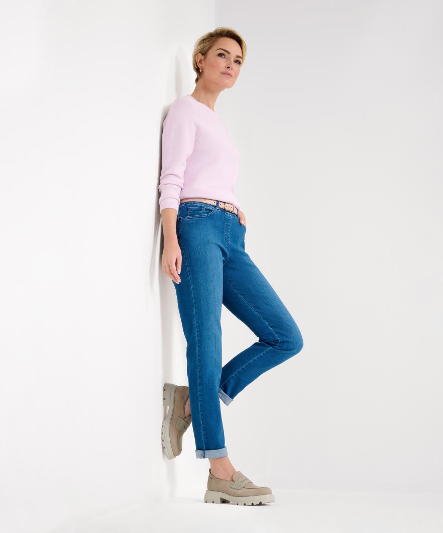 Side view  pink long sleeve top and blue jeans with a high waist and slim fit. She is also wearing a pair of tan shoes.