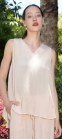 A woman wearing a beige viscose crepe de chine top with a V-neckline, crossover detail, and a dipped curve hem, standing in a garden setting.