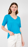 Front View blue carry tee with V-neck and perforated embroidery on the collar and sleeve cuffs paired with white trousers.