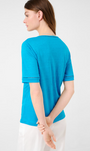 Back Viewblue carry tee with V-neck and perforated embroidery on the collar and sleeve cuffs paired with white trousers.