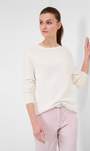 A woman wearing a white knitted sweater with a round neckline and long sleeves, paired with pink pants with a geometric pattern.