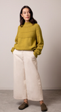 Woman wearing a mustard yellow sweater and white pants.