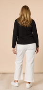 Woman wearing a black top and white pants against a beige background