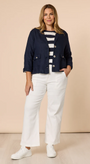 Woman wearing a navy jacket, striped shirt, and white pants against a beige background