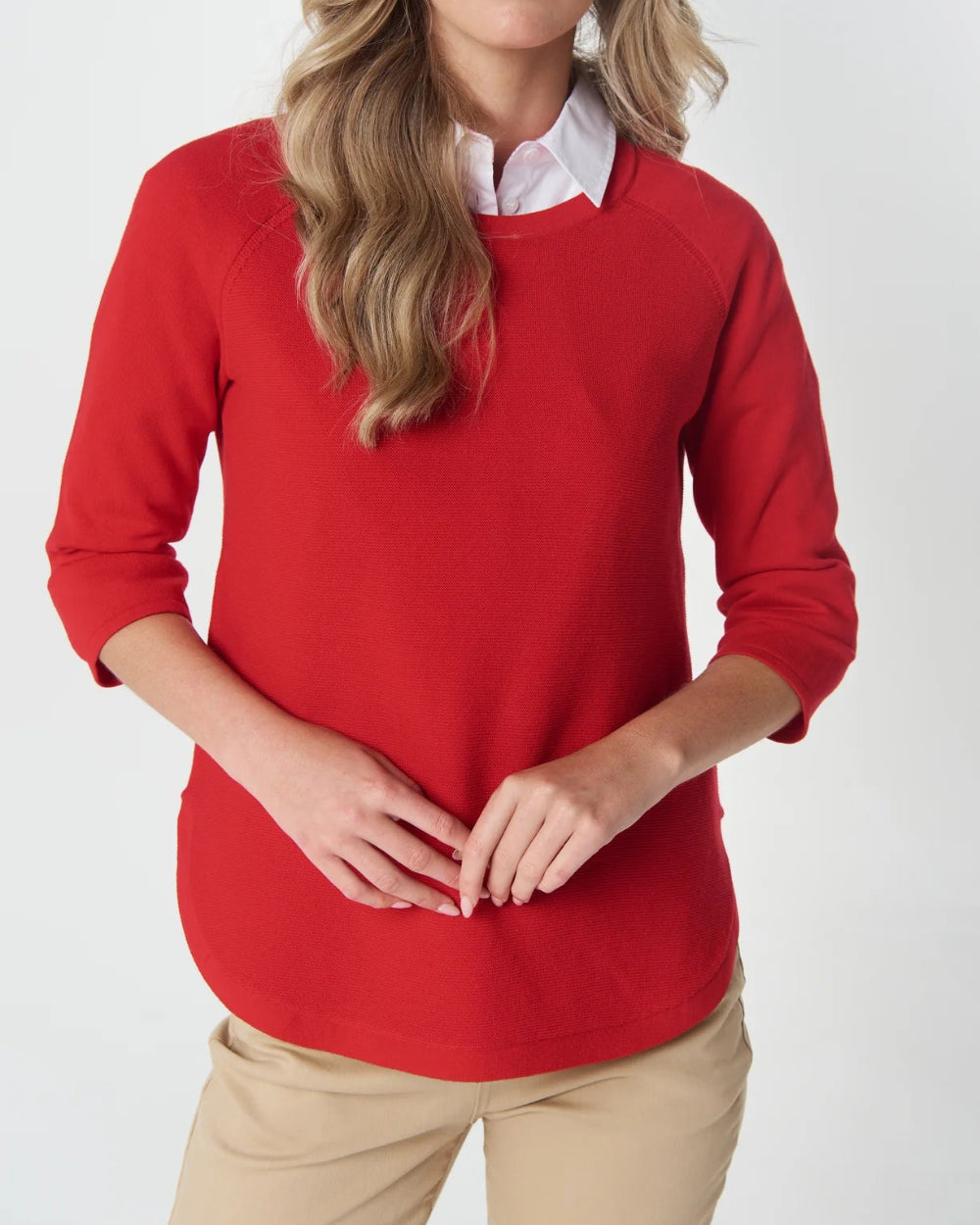 bright red crewneck sweater with three quarter sleeves, layered over a white collared shirt and paired with beige pants. 