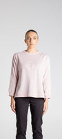 Person wearing a light pink long-sleeve top with a logo on a white background
