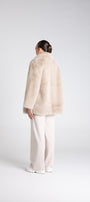 Person wearing a beige fur coat and pants on a white background