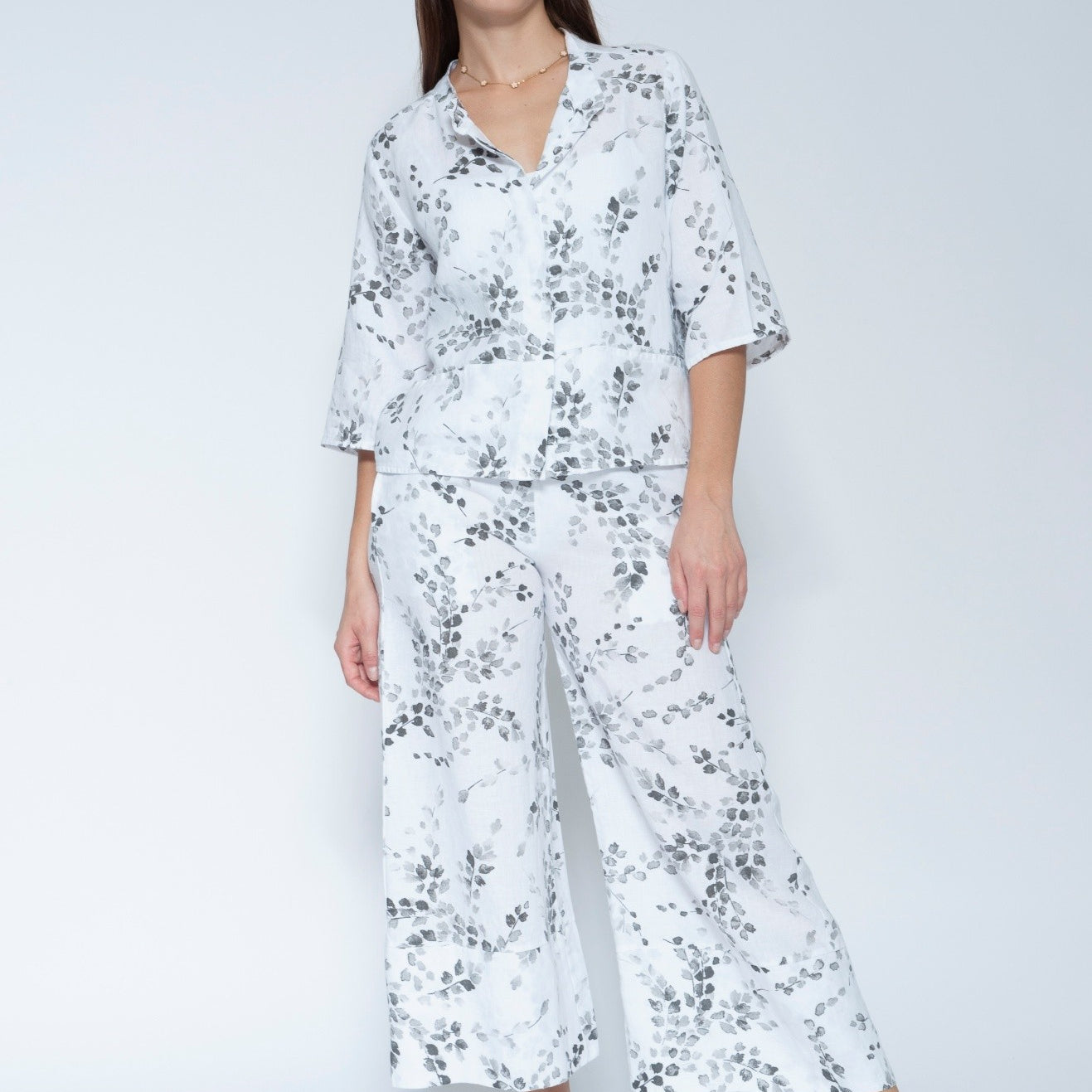  Front view  matching two piece jacket and pant set with a white base and black floral print, featuring a short sleeve button up top and wide leg pants, paired with black slide sandals.