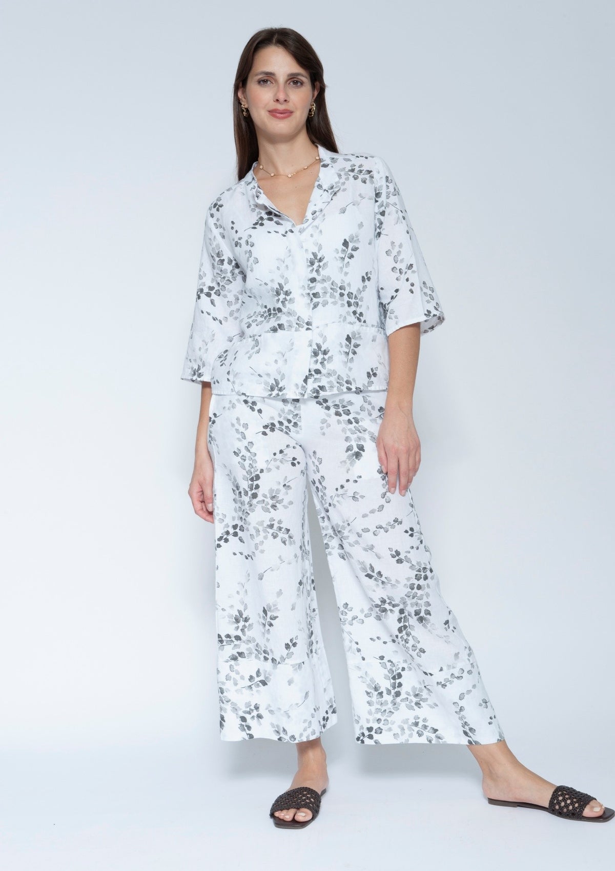  Front view  matching two piece jacket and pant set with a white base and black floral print, featuring a short sleeve button up top and wide leg pants, paired with black slide sandals.