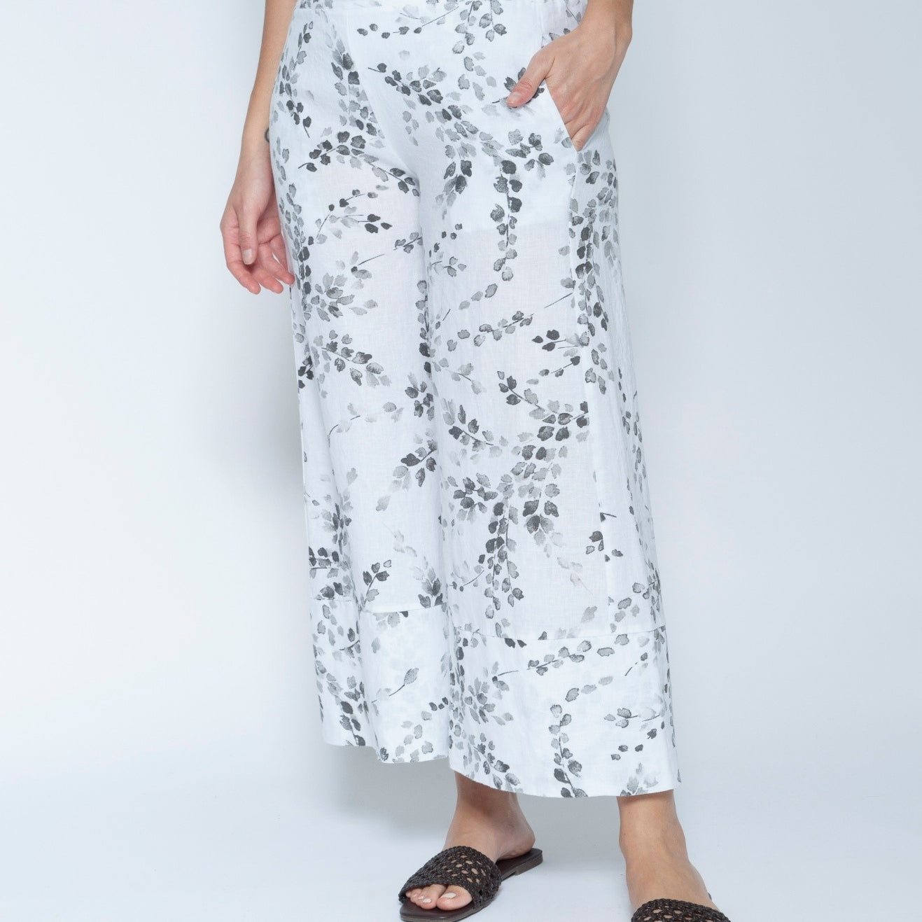 White wide leg cropped pants with a gray leafy vine pattern, modeled with a white sleeveless top and black slide sandals.