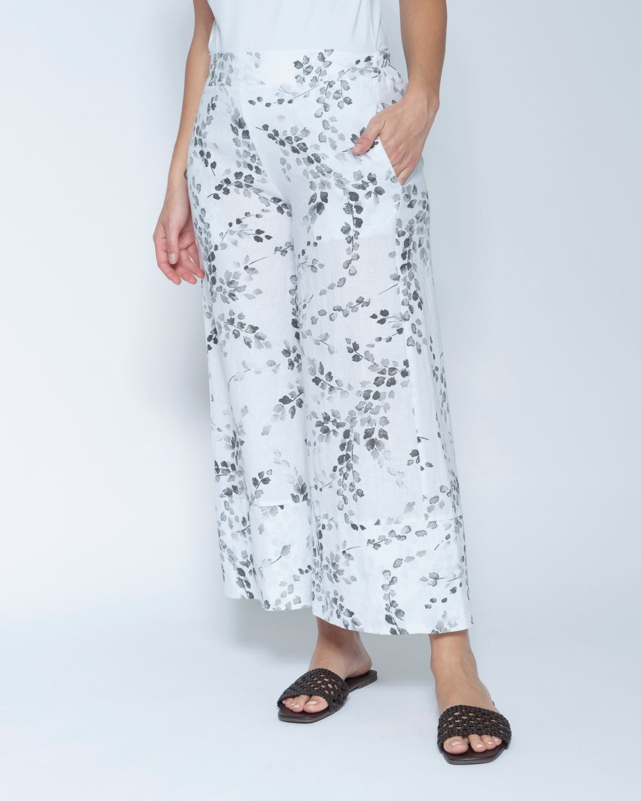 White wide leg cropped pants with a gray leafy vine pattern, modeled with a white sleeveless top and black slide sandals.