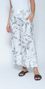 White wide leg cropped pants with a gray leafy vine pattern, modeled with a white sleeveless top and black slide sandals.