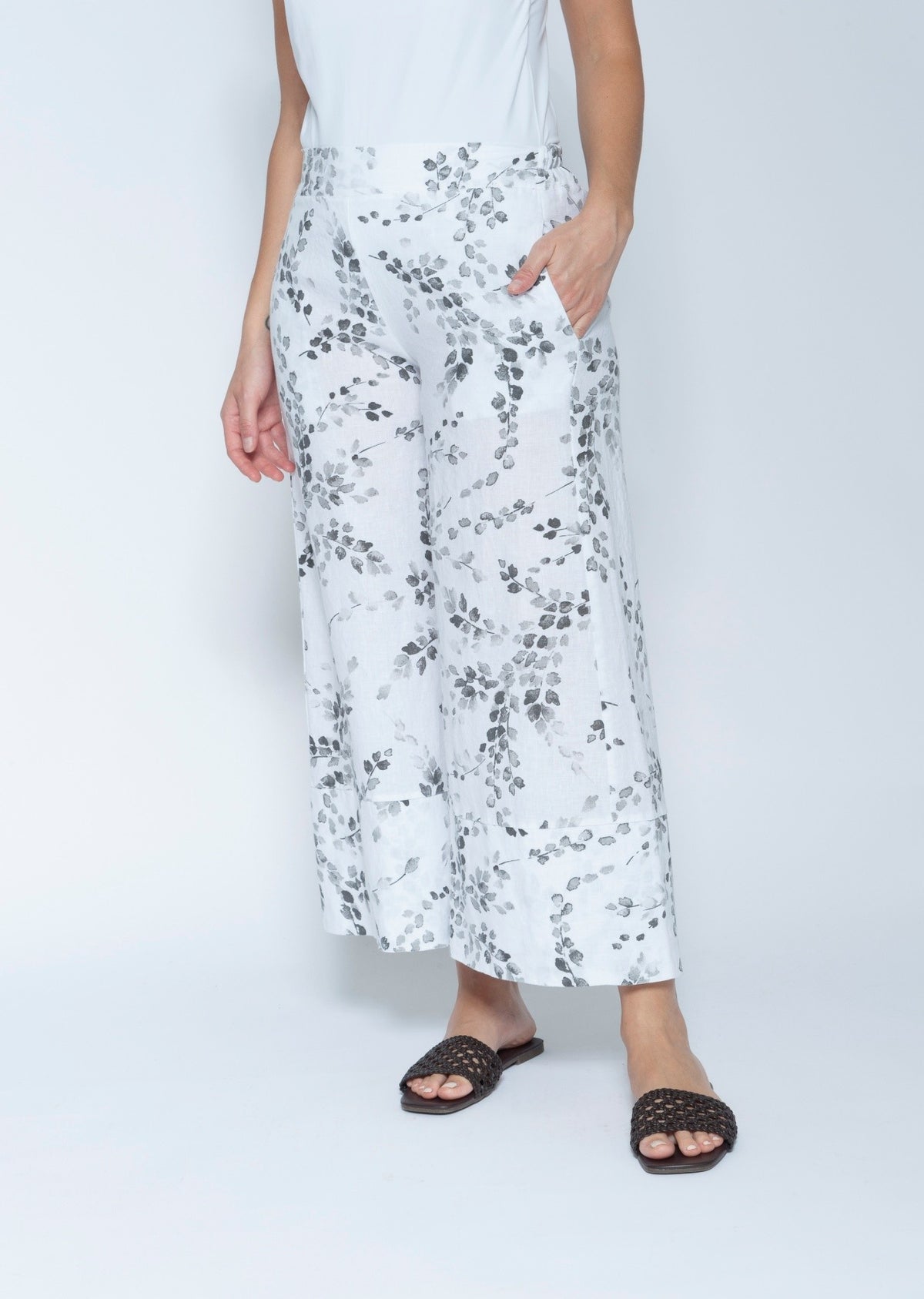 White wide leg cropped pants with a gray leafy vine pattern, modeled with a white sleeveless top and black slide sandals.