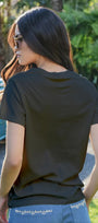 Woman wearing a black t-shirt with a blurred background of a blue truck and greenery