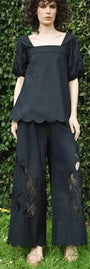 Person wearing a black embroidered outfit standing against a green hedge.