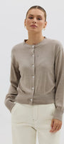 Woman wearing a beige cardigan and white pants against a plain background