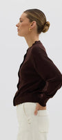 Woman wearing a brown blouse and white pants against a light background