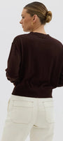 Person wearing a brown sweater and white pants on a light gray background